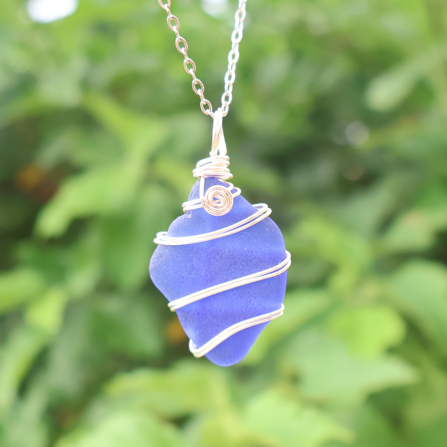 Blue sea glass necklace on a chain against a green leafy background
